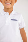 A smiling child wears The Beaufort Bonnet Company’s Michigan Prim & Proper Polo in Worth Avenue White, featuring the Michigan logo embroidered in blue on the chest. The background is plain and light.