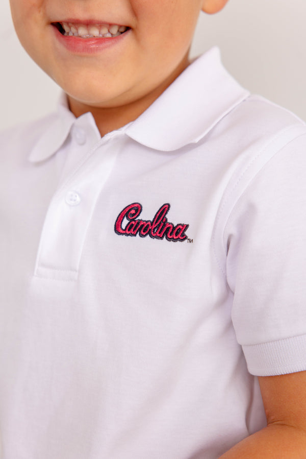 A child smiles while wearing The Beaufort Bonnet Company’s South Carolina Prim & Proper Polo in Worth Avenue White, featuring “Carolina” embroidered in red on the chest.