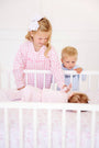A young girl in a pink gingham sibling reveal shirt and a boy in a Cassidy Comfy Crewneck - Buckhead Blue Gingham with Nantucket Navy Big Brother look down at a baby lying in a white crib.