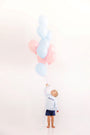 A young boy wears a Cassidy Comfy Crewneck - Buckhead Blue Gingham with Nantucket Navy Big Brother shirt while holding a large bunch of blue and pink balloons for a sibling reveal.
