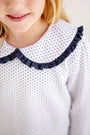 A young girl is wearing The Beaufort Bonnet Company’s Maude’s Ruffle Cassidy Comfy Crewneck in Nantucket Navy Microdot with Worth Avenue White. Her blonde hair peeks out as she smiles softly, highlighting the shirt’s charming ruffle collar and comfy style.