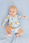 A smiling baby lies on a light blue blanket, wearing The Beaufort Bonnet Company’s Long Sleeve Patton Play Bubble in the Candy & Critters (Buckhead Blue) design, featuring festive Halloween-themed illustrations.