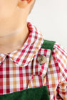 Close-up of a child wearing The Beaufort Bonnet Company’s Long Sleeve Peter Pan Collar Shirt & Onesie in Easton Pond Plaid, paired with green corduroy overalls fastened with a tan button. The child’s face is partially out of frame.