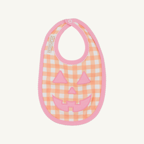 A fall baby essential, the Burp Me Bib - Seashore Sherbet Gingham & Hamptons Hot Pink by The Beaufort Bonnet Company features an orange and white gingham pattern with a hot pink trim and a cheerful pink jack-o-lantern face design on the front.