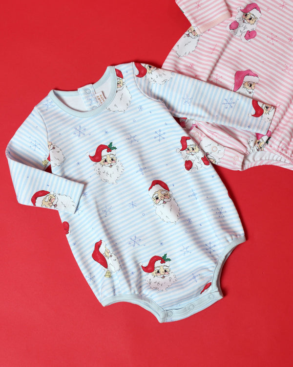 Two Long Sleeve Patton Play Bubble - Dear Santa (Buckhead Blue Stripe) rompers featuring a Santa Claus and snowflake pattern, one in blue stripes and one in pink stripes, against a red background.