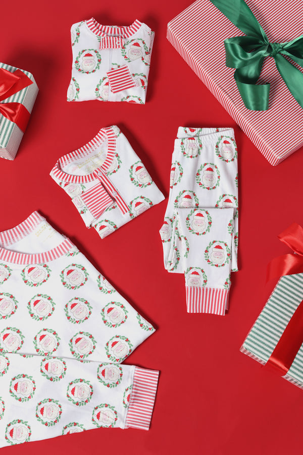 Folded and laid-out Knox’s Night Night - North Pole Portrait with Richmond Red Stripe pajamas by The Beaufort Bonnet Company are displayed on a red background, surrounded by wrapped gifts with green and red ribbons.