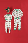 Two Sutton’s Sweet Dream Sets in The Beaufort Bonnet Company’s Serious Santa Business print—one footed and one not—are laid out on a red background next to a gift wrapped with a green ribbon.