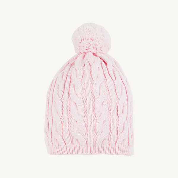 The Collins Cable Knit Hat in Palm Beach Pink from The Beaufort Bonnet Company features a classic cable knit pattern throughout and is topped with a large pompom. This girls’ winter hat is displayed against a plain white background.
