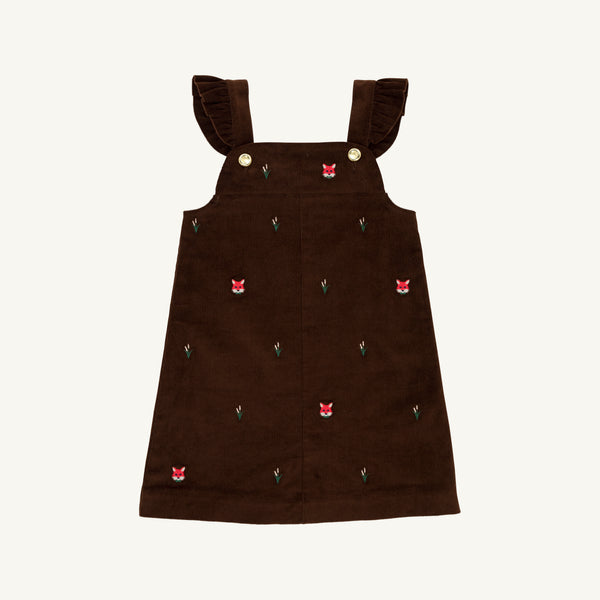 The Beaufort Bonnet Company Critter Julia Jumper in Chelsea Chocolate corduroy features ruffled shoulder straps, gold buttons, and small embroidered red fox faces with green plants scattered across the fabric.