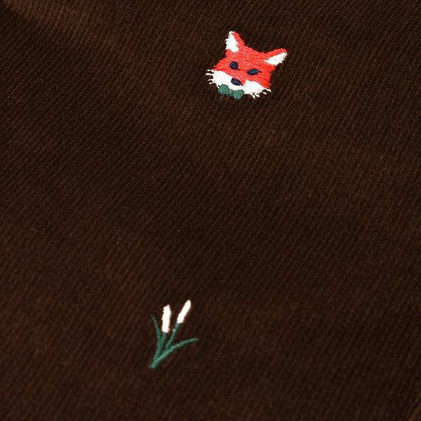 A close-up of The Beaufort Bonnet Company Critter Julia Jumper in Chelsea Chocolate corduroy, showcasing the fox embroidery—a red fox head alongside a delicate patch of white flowers with green stems.