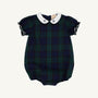 The Beaufort Bonnet Company’s Bedford Bubble in Berwick Black Watch features short puffy sleeves, a Worth Avenue White Peter Pan collar adorned with Nantucket Navy Bows, and elastic leg openings; the romper showcases dark green and navy blue tones.