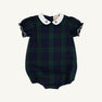 The Beaufort Bonnet Company’s Bedford Bubble in Berwick Black Watch features short puffy sleeves, a Worth Avenue White Peter Pan collar adorned with Nantucket Navy Bows, and elastic leg openings; the romper showcases dark green and navy blue tones.