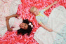 Two children—one with curly dark hair and the other with short blond hair—smile while lying on their backs amid a sea of pink balloon shapes, cozily wrapped in The Beaufort Bonnet Company’s Silent Night Throw - Ice Cream Daydream (Blueberry Blue). Their patterned blankets feature colorful designs, and both appear happy and relaxed.