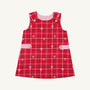 The Beaufort Bonnet Company’s Janie Jumper in Torrington Tartan with Pier Party Pink is a girls’ flannel dress for toddlers, featuring a sleeveless red tartan design, accented with small white bows, pink side bands, and gold buttons on the shoulders and waist. The dress is shown against a plain white background.