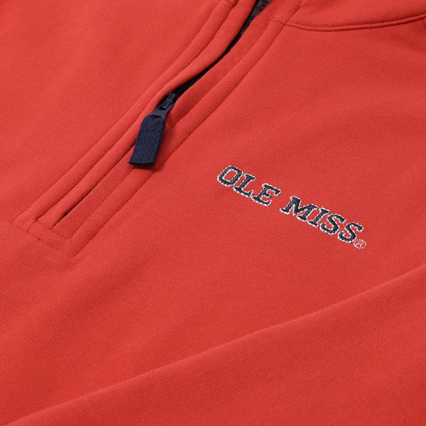 A close-up of The Beaufort Bonnet Company’s Ole Miss Hayword Half-Zip in Ole Miss Red with Nantucket Navy showcases an embroidered logo in white and blue thread on the chest, complemented by a navy zipper pull near the top—perfect for effortless game day layering.