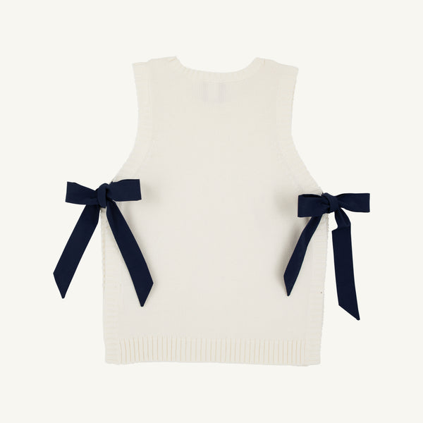 Introducing the Shae Sweater Vest - Palmetto Pearl with Nantucket Navy by The Beaufort Bonnet Company: a sleeveless white knit vest with ribbed edges, adorned with two navy blue ribbon bows tied at the sides. Made from 100% cotton, this sweater is a charming addition to any girl’s autumn wardrobe.