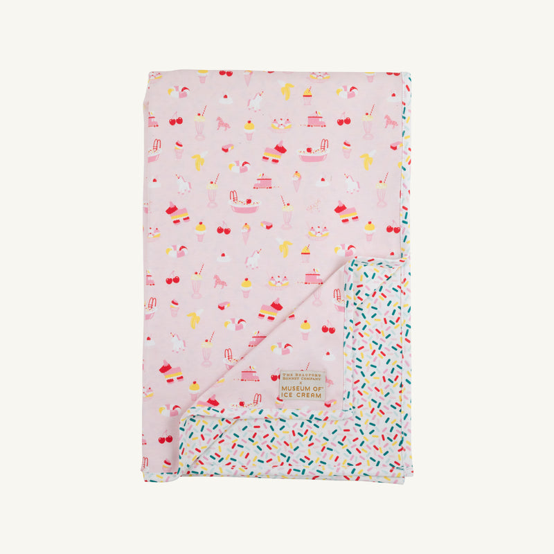 Introducing the Silent Night Throw - Ice Cream Daydream (Strawberry Pink) by The Beaufort Bonnet Company: a pink Pima cotton throw blanket with colorful ice cream-themed illustrations on one side and a vibrant sprinkle pattern on the reverse. It features a soft finish and a small fabric label that reads Museum of Ice Cream.