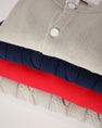 A stack of Cambridge Cardigan - Grantley Gray, navy blue, and bright red cardigans folded for a little one’s wardrobe.
