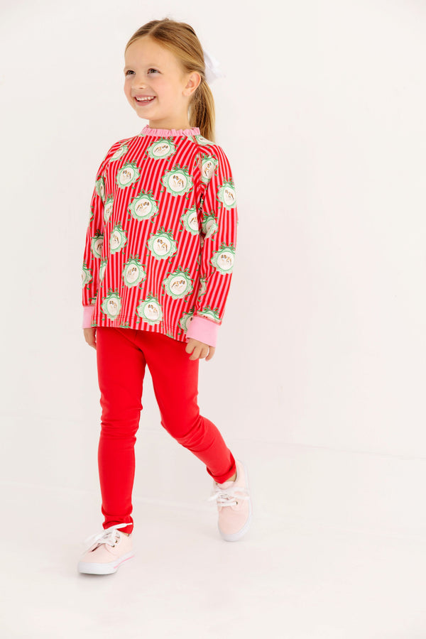 A girl wears a Cassidy Comfy Crewneck - Distinguished Doggies with Hamptons Hot Pink featuring red-and-white striped dog illustrations, paired with solid red leggings and light pink sneakers for her winter wardrobe.