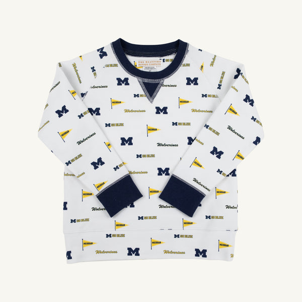 The Beaufort Bonnet Company’s Michigan Cassidy Comfy Crewneck - Bold in Blue with Michigan Blue offers cozy comfort for kids and features navy cuffs and collar, adorned with repeating University of Michigan M logos, pennants, and “Wolverines” text in blue and yellow for spirited school pride.