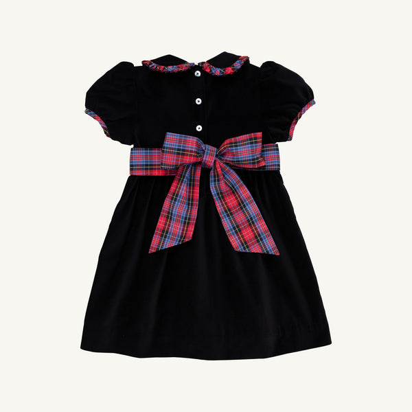 Introducing the Cindy Lou Sash Dress - Newport Night Velveteen with Bucktown Tartan by The Beaufort Bonnet Company. Perfect for holiday occasions, this charming children’s dress features short sleeves, white buttons, and a plaid Bucktown Tartan collar trim. A large red and blue plaid sash bow at the waist adds a festive touch, while its soft cotton velveteen construction ensures comfort. Displayed on a plain background.