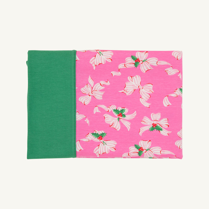 A closed notebook with a green spine and a pink cover, adorned with the Bows of Holly pattern in white and pink flowers with green centers—an enchanting design inspired by The Beaufort Bonnet Company’s Fresh Face Pillowcase - Bows of Holly with Kiawah Kelly Green—set against a plain background.