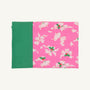 A closed notebook with a green spine and a pink cover, adorned with the Bows of Holly pattern in white and pink flowers with green centers—an enchanting design inspired by The Beaufort Bonnet Company’s Fresh Face Pillowcase - Bows of Holly with Kiawah Kelly Green—set against a plain background.
