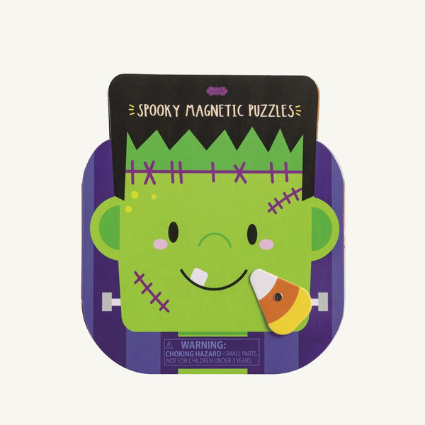 A cartoon Frankenstein face appears on a purple background labeled “Monster Magnetic Puzzle Book - Mud Pie” by The Beaufort Bonnet Company, featuring a candy corn magnet on its cheek. This magnetic puzzle is a fun travel toy and creative activity. Warning: Choking hazard—small parts. Not for children under 3 years.