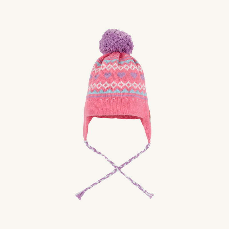 The Parrish Pom Pom Hat by The Beaufort Bonnet Company is a girls’ winter hat in Winter Park Pink, featuring a purple pom-pom, earflaps with braided strings, and a charming Fair Isle hearts pattern in light blue, white, and pink around the crown.