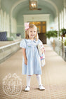 A young girl in a light blue The Beaufort Bonnet Company outfit with a pink bow in her hair and Jefferies High Class Knee Socks in white holds a stuffed bunny while standing in a bright, elegant hallway.