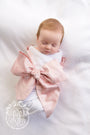 A newborn baby wrapped in a Southern Blush Silk Bow Swaddle ®, featuring white fabric and a large, blush-pink silk bow across the chest for beautiful newborn pictures.