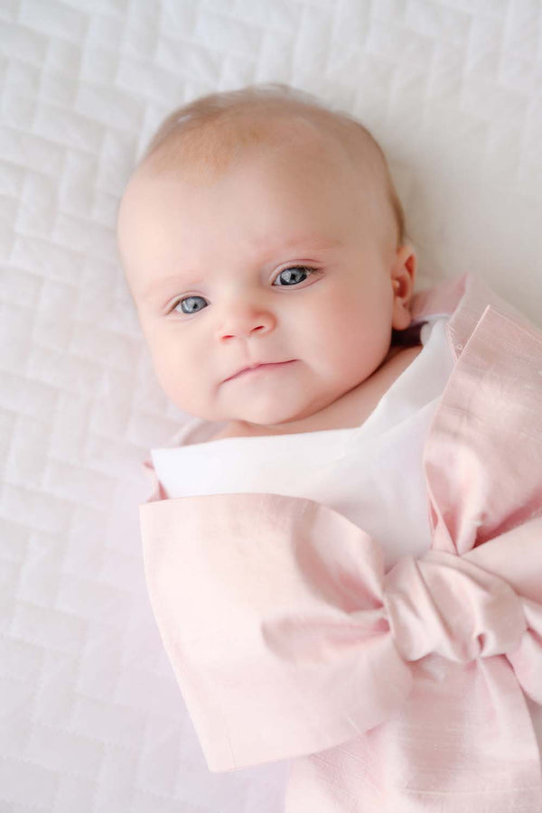 A newborn baby wrapped in a light pink Bow Swaddle ® - Southern Blush Silk, perfect for keepsake pictures.