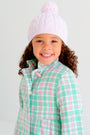A smiling young girl wears The Beaufort Bonnet Company’s Collins Cable Knit Hat in Palm Beach Pink and a pastel plaid coat featuring green, pink, and white, standing against a plain light background.