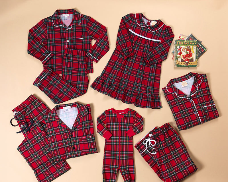A collection of matching family Christmas pajamas, including Let Me Lounge Set - Society Prep Plaid with Worth Avenue White children’s sets and a girls’ nightgown, arranged around a copy of The Night Before Christmas book.