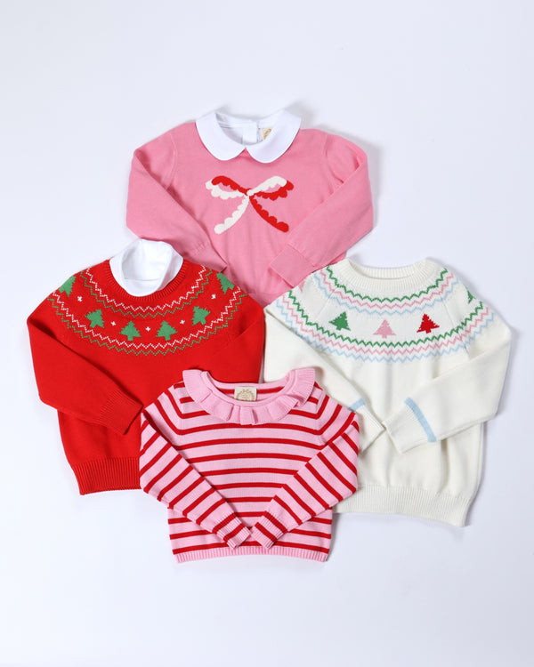 Four children’s cotton sweaters on a white background: a pink sweater with a bow, an Isaac’s Fair Isle Sweater - Richmond Red with Christmas Trees, a white sweater with colorful trees, and a red and pink striped sweater.