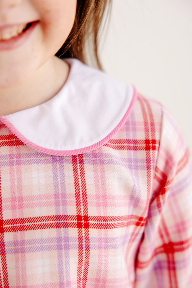 A child wears The Beaufort Bonnet Company’s Lindy’s Lunch Dress in Broadway Play Plaid with Worth Avenue White, a long-sleeved plaid dress with a white rounded collar trimmed in pink.