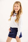 A girl wearing a white V-neck sweater with red and navy trim and a Stevi Skirt - Nantucket Navy Corduroy with an adjustable waistband.