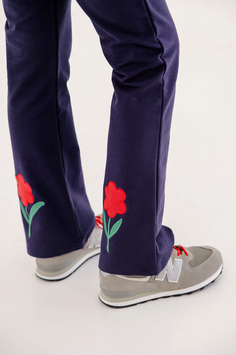Patty Pants - Nantucket Navy & Richmond Red with Flowers in a navy blue bootcut style with embroidered flowers on the lower legs, worn with grey sneakers.