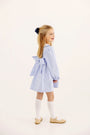 A young girl wears The Beaufort Bonnet Company Long Sleeve Dollie Mae Dress - Park City Periwinkle Ticking Stripe & Worth Avenue White, paired with white knee-high socks and beige Mary Jane shoes.