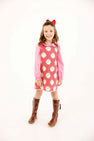 A girl wears a red and white striped Annie Apron Dress - Distinguished Doggies with Hamptons Hot Pink over a pink long-sleeve collared shirt, paired with brown knee-high boots and a red hair bow.