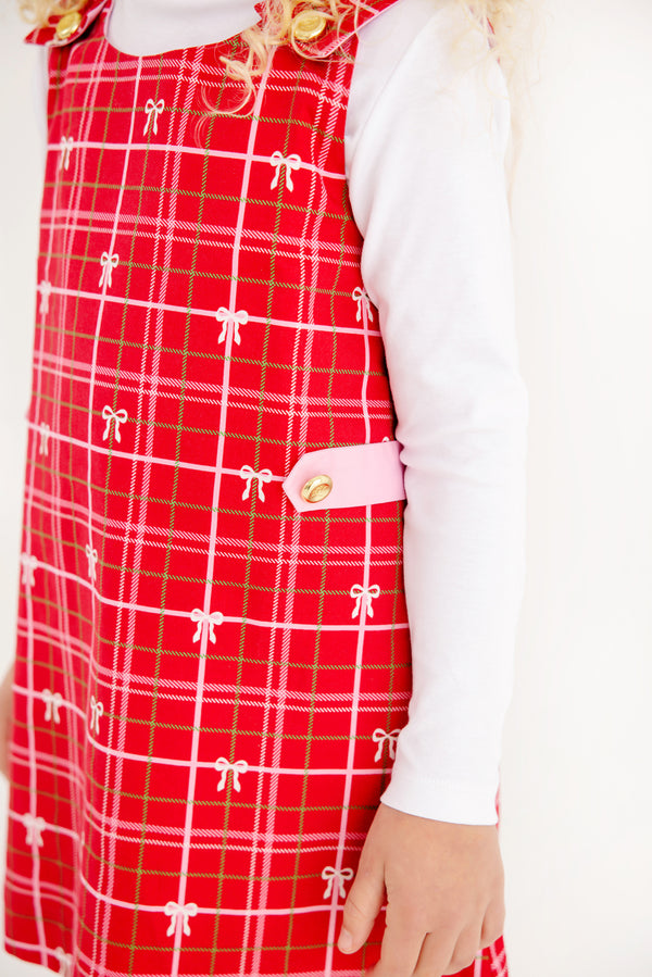 A young child wearing The Beaufort Bonnet Company’s Janie Jumper in Torrington Tartan with Pier Party Pink, layered over a long-sleeved white shirt, standing against a white background.