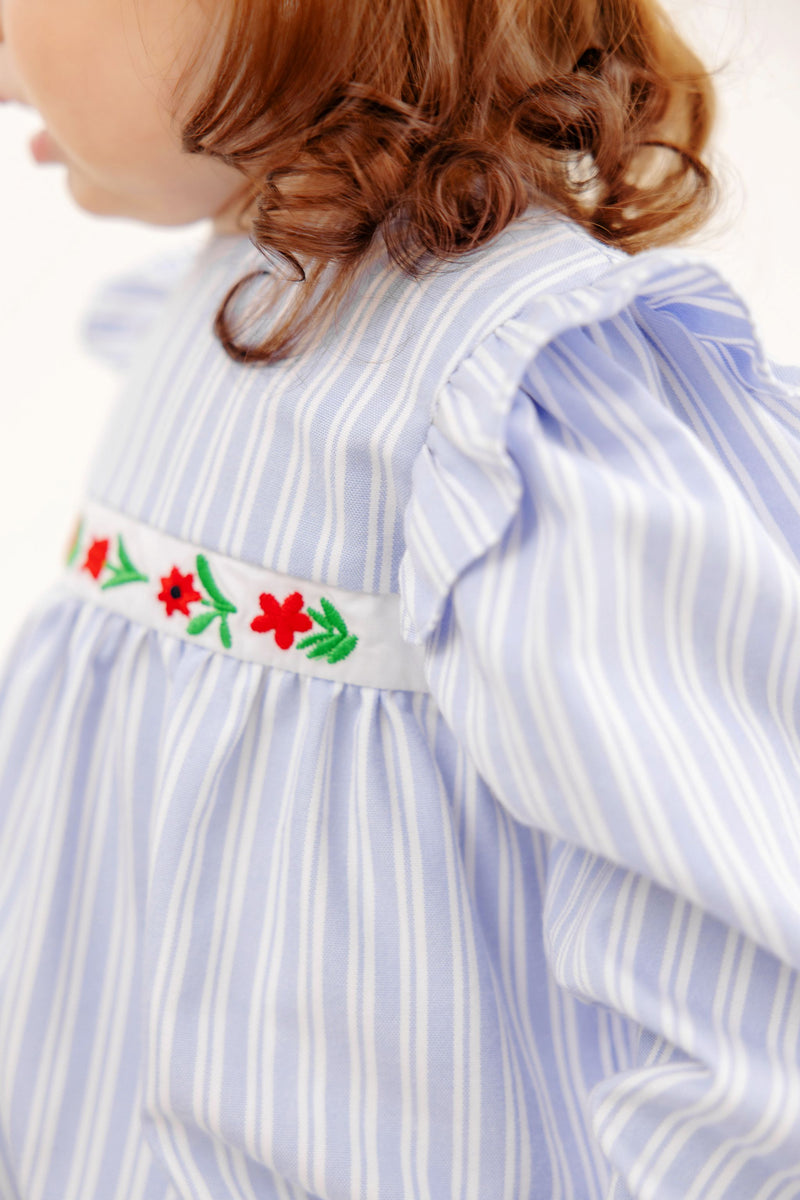 The Long Sleeve Ruehling Ruffle Bubble - Park City Periwinkle Ticking Stripe & Worth Avenue White is a long-sleeved light blue and white striped romper with ruffled shoulders and a white band embroidered with red and green flowers at the waist.