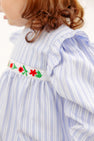 The Long Sleeve Ruehling Ruffle Bubble - Park City Periwinkle Ticking Stripe & Worth Avenue White is a long-sleeved light blue and white striped romper with ruffled shoulders and a white band embroidered with red and green flowers at the waist.