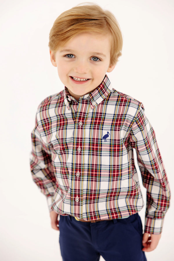 A young boy smiling in a Dean’s List Dress Shirt - Paris Pike Plaid with Nantucket Navy Stork, featuring a long-sleeved button-down design with a small stork embroidery on the chest.