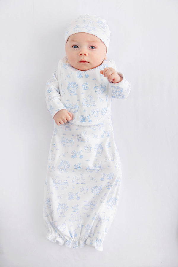 A baby dressed in The Beaufort Bonnet Company’s Sir Proper’s Sweet Arrival (Beale Street Blue) Bundle – a charming everyday set complete with a white hat, matching bib, and light blue layette gown – lies contentedly on a white background, gazing up with wide-eyed wonder. This adorable scene captures the perfect baby shower gift.