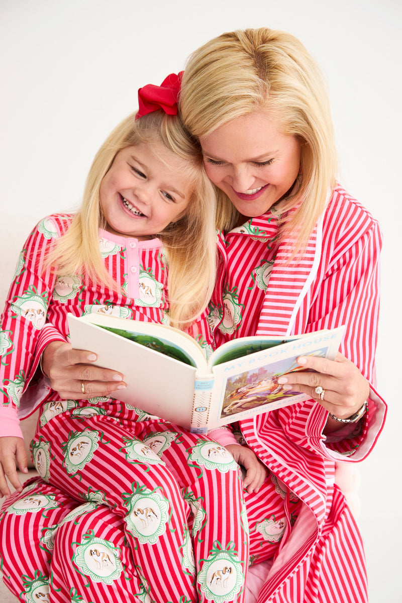 A woman and a young girl read a book together while wearing matching Payton Pajama Set - Distinguished Doggies with Hamptons Hot Pink cotton pajamas featuring dog prints.