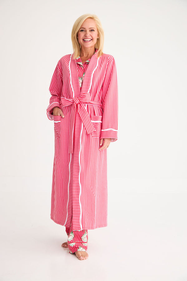 A smiling woman wears a cozy Rest Awhile Robe - Richmond Red & Hamptons Hot Pink in red and white stripes with white piping over matching pajama pants.
