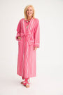 A smiling woman wears a cozy Rest Awhile Robe - Richmond Red & Hamptons Hot Pink in red and white stripes with white piping over matching pajama pants.