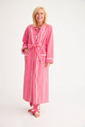 A smiling woman wears a cozy Rest Awhile Robe - Richmond Red & Hamptons Hot Pink in red and white stripes with white piping over matching pajama pants.