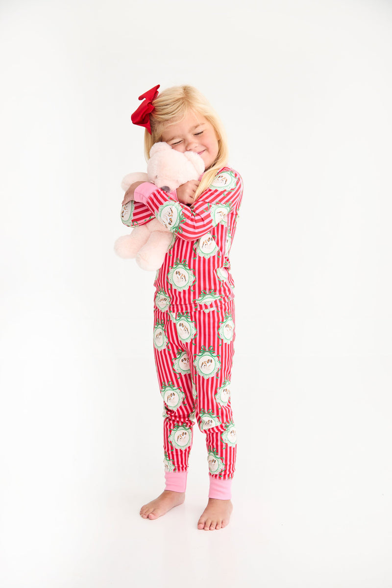 A young girl wears a Payton Pajama Set - Distinguished Doggies with Hamptons Hot Pink while hugging a plush toy.